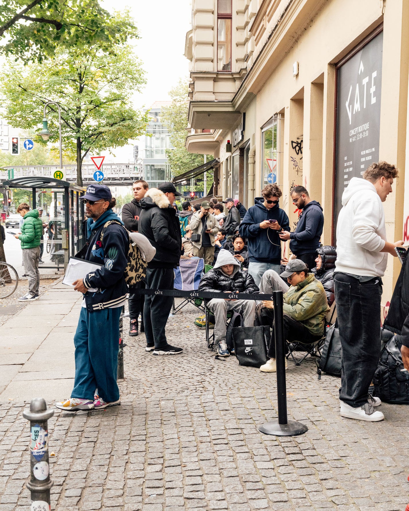 People waiting in line on a city street with a building and tree in the background. RECAP: Tom Sachs x Nike Mars Yard 3.0