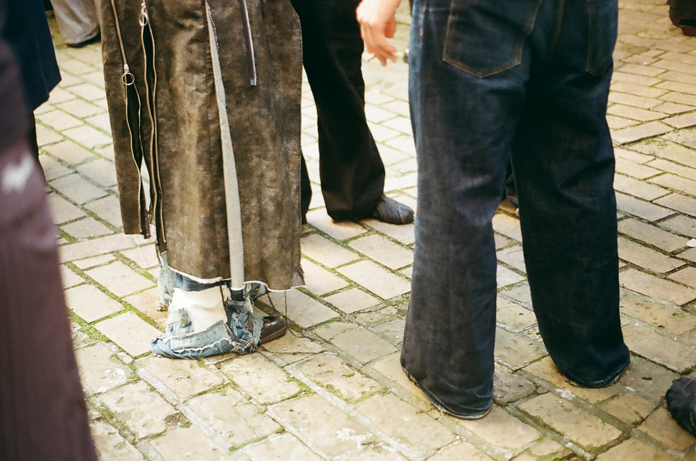 Puma x Non Faith Studios Event Recap. Person wearing a brown coat and dark jeans on a brick pavement