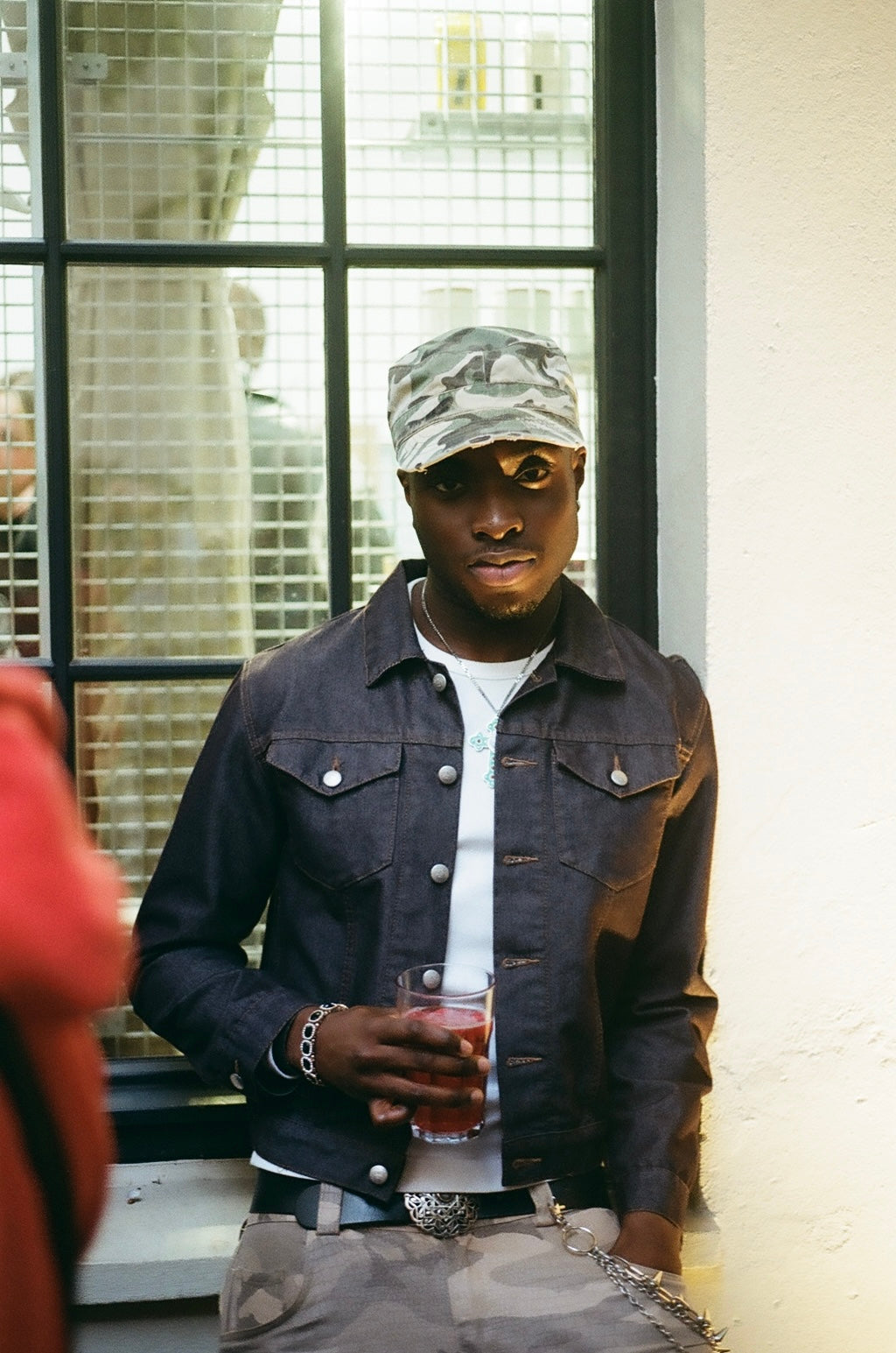 Puma x Non Faith Studios Event Recap.
Man wearing a denim jacket and cap, holding a drink in front of a window.