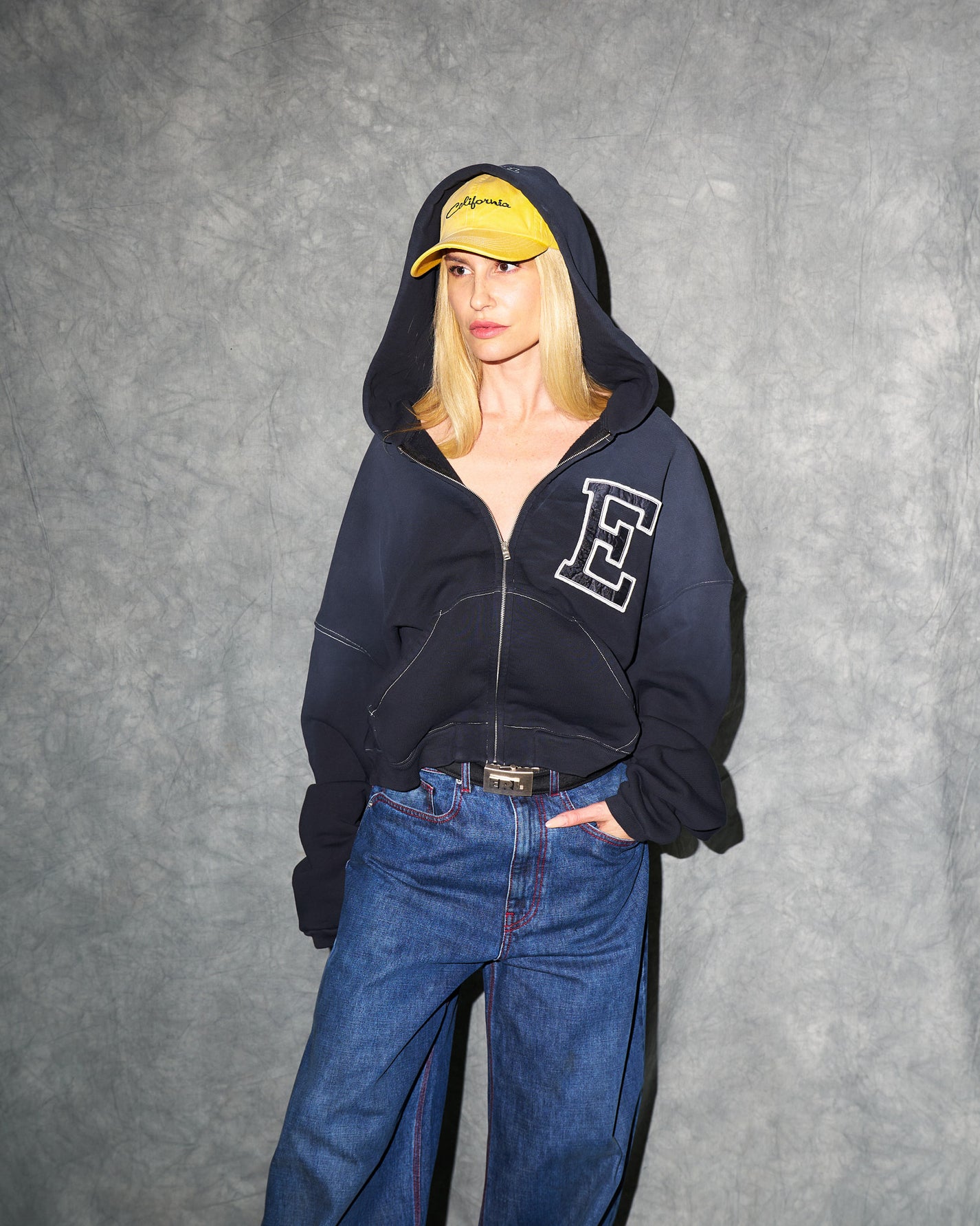 A woman wearing ERL clothing, a zip hoodie, denim and a cap
