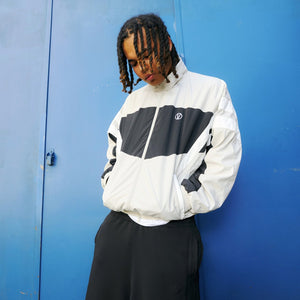 image of a young man wearing a track jacket in beige and black with white stripes by VETEMENTS and wide black pants