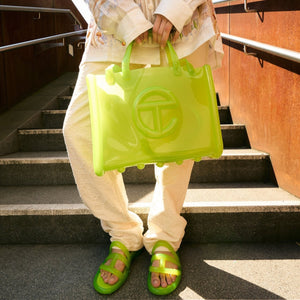 woman on a staircase carrying a light green jelly shopping bag